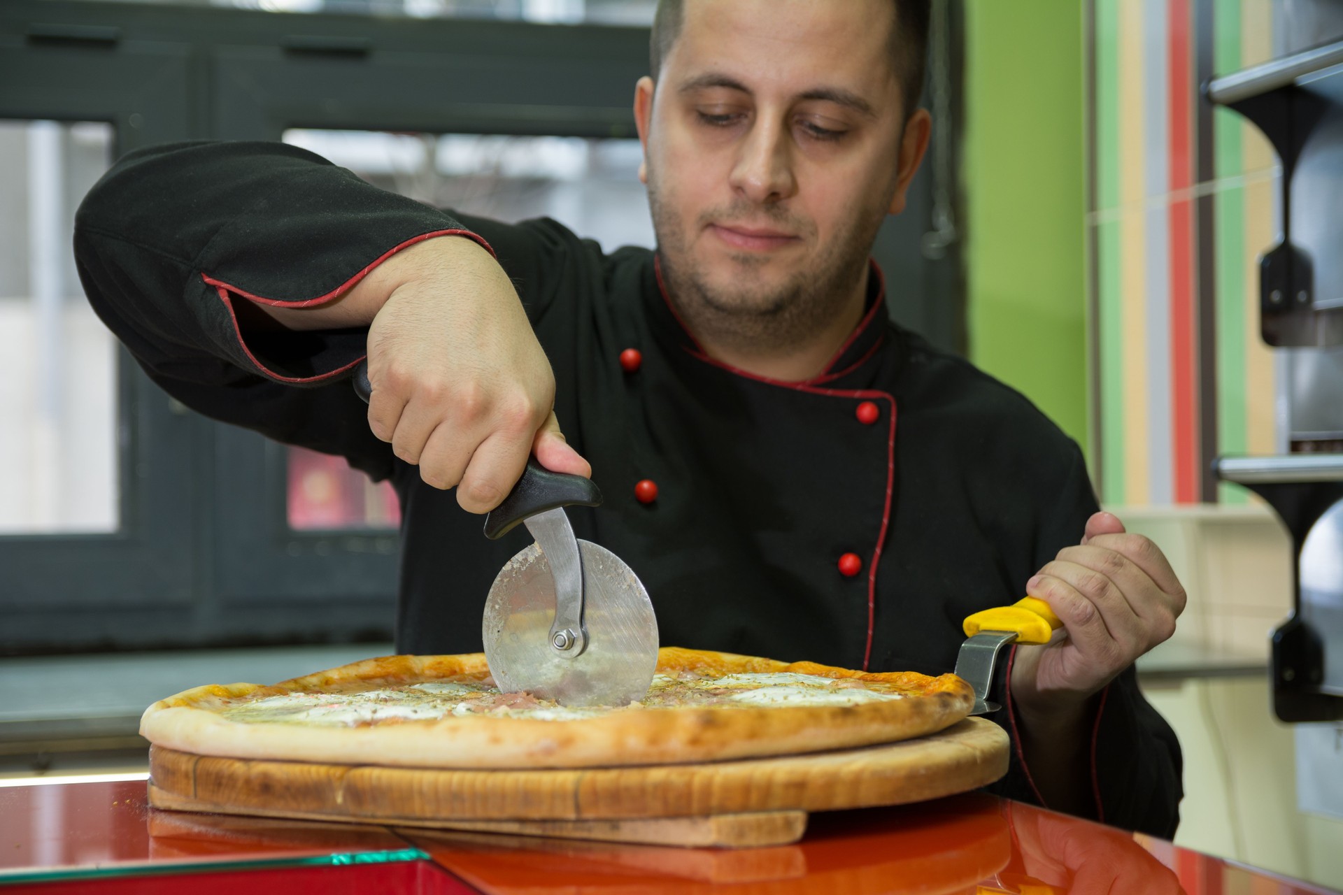 Pizza Chef in black uniform cutting Pizza on a wooden board - Image